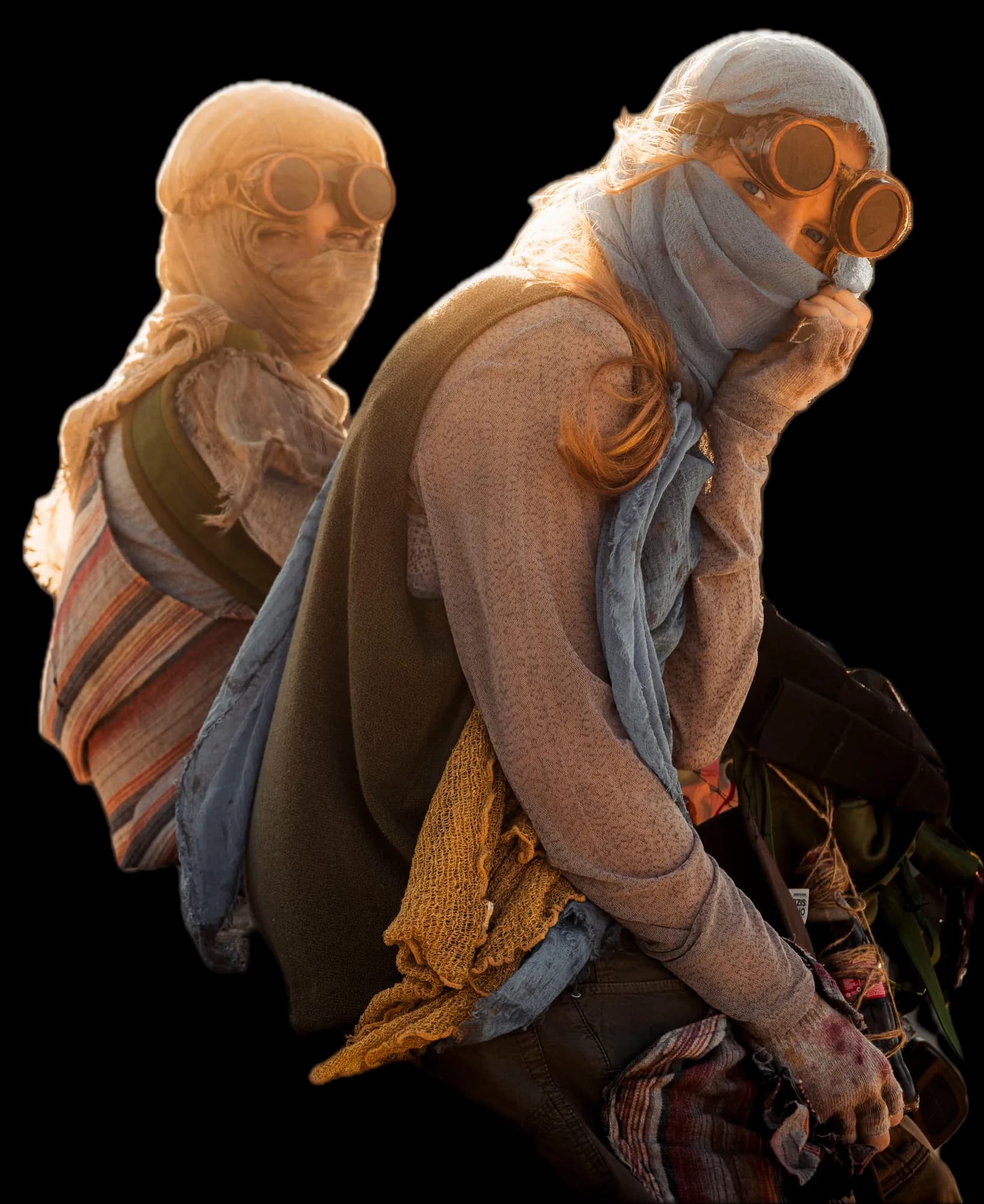 Two young people sit on a rock in golden backlight. The woman in front looks into the camera over her scarf, wearing copper goggles and a mustard knitted scarf. Behind her sits a figure wrapped in gauze.